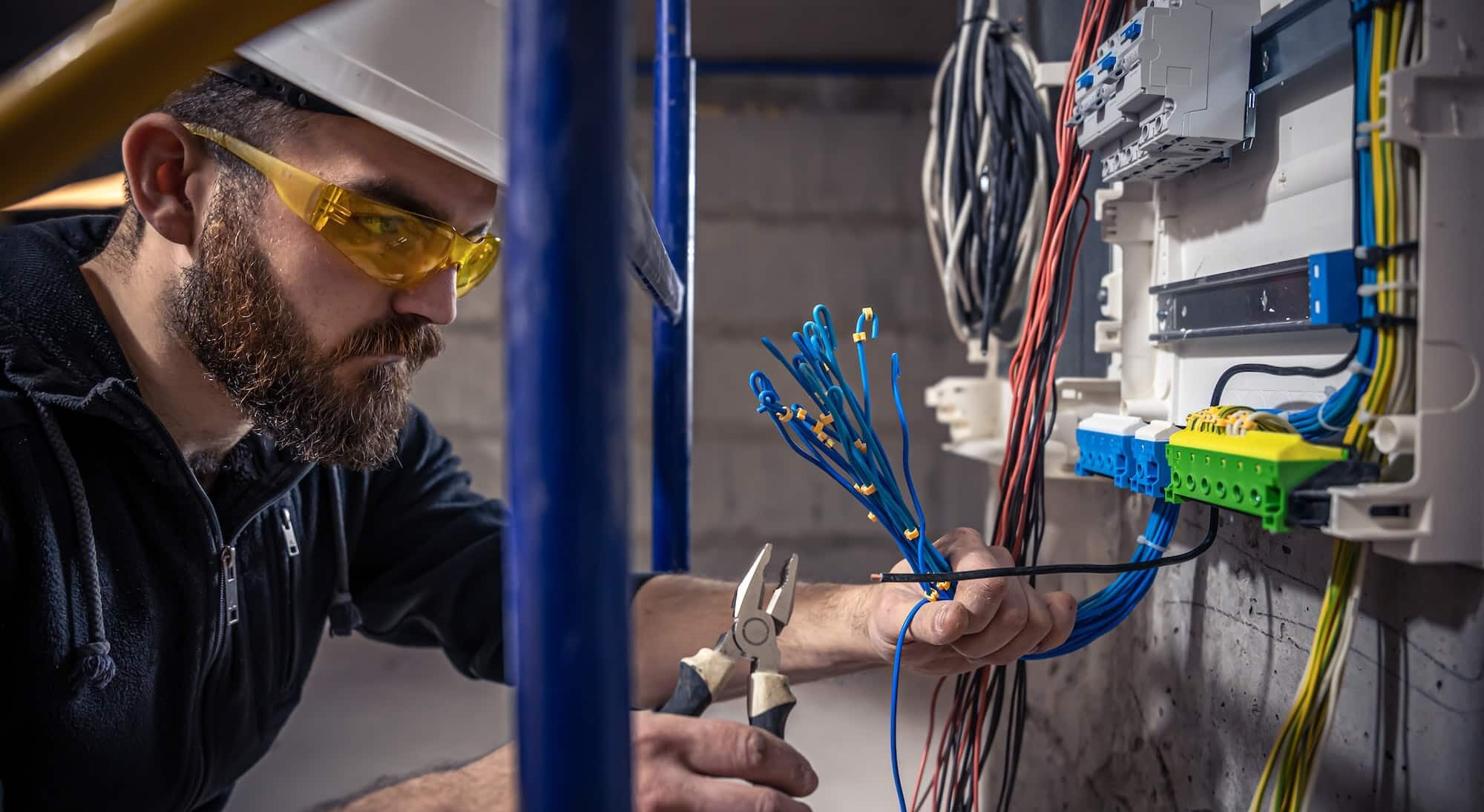 A male electrician works in a switchboard with an electrical connecting cable.