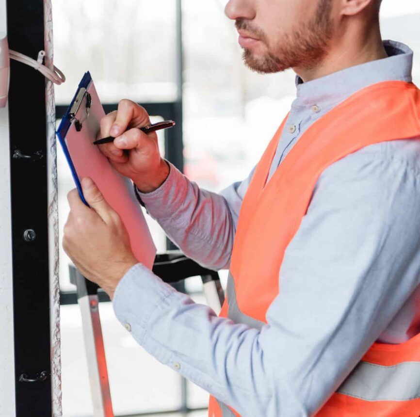 cropped view of fireman standing near fire alarm while holding clipboard and pen