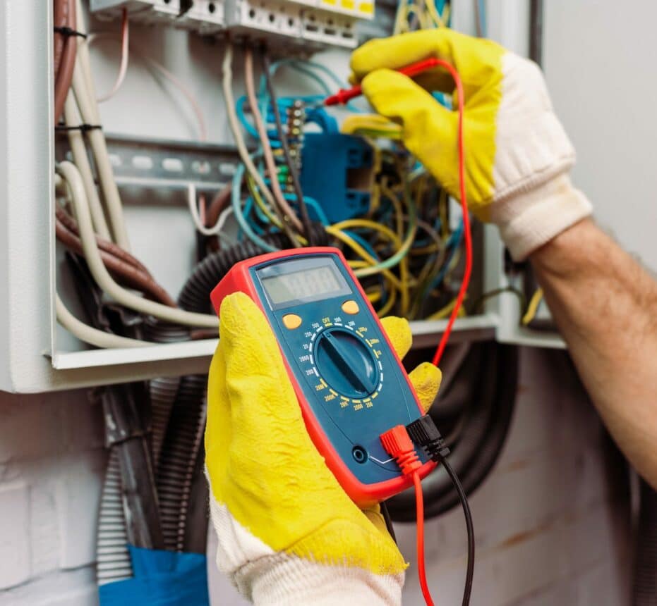 Cropped view of workman in gloves using multimeter while checking voltage of electric panel