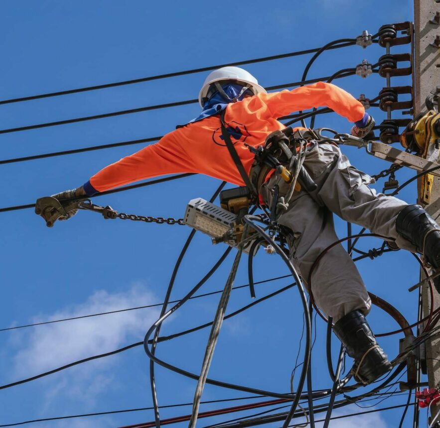 Electrician with work tools is installing cable lines and electrical system on power pole