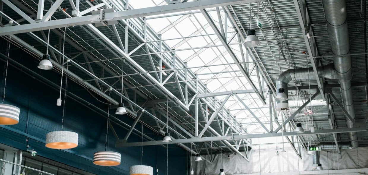 Metal roof structure of a large building, indoors. Built-in windows at the top for lighting