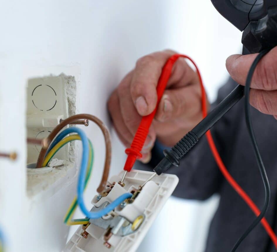 An electrician using a multimeter to check voltage in a domestic receptacle/socket outlet.